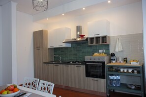 A modern kitchen with wooden cabinets, a gas stove, an oven, and a small dining area with a table and chairs. - Casa Graziosa, an authentic corner of Campania (Ercolano)