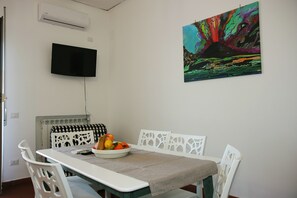 Ein Essbereich mit Tisch, Stühlen, einer Obstschale und einem Bild an der Wand.