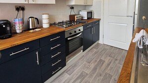 Cocina compacta con armarios blancos, microondas, estufa y cafetera.