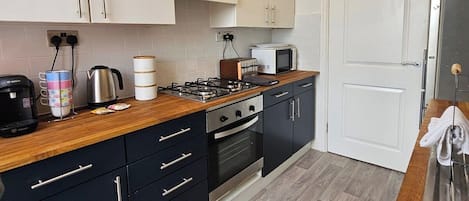 Cocina compacta con armarios blancos, microondas, estufa y cafetera.