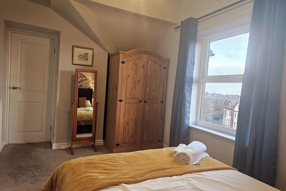A bedroom with a bed, a wardrobe, a mirror, and a window with a view.