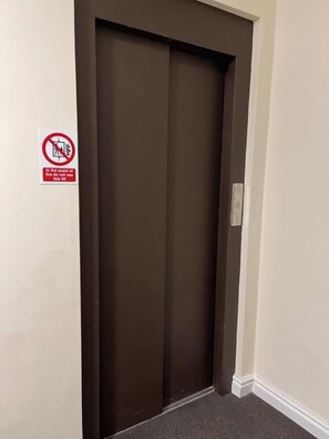 Geschlossene Aufzugtür mit einem Rauchverbotsschild an der angrenzenden Wand.