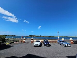 Ein Parkplatz mit drei Autos, blauem Himmel und einem Gewässer im Hintergrund.