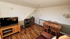 Una sala de estar con televisor sobre un mueble de madera, una mesa de comedor con sillas y un sofá.