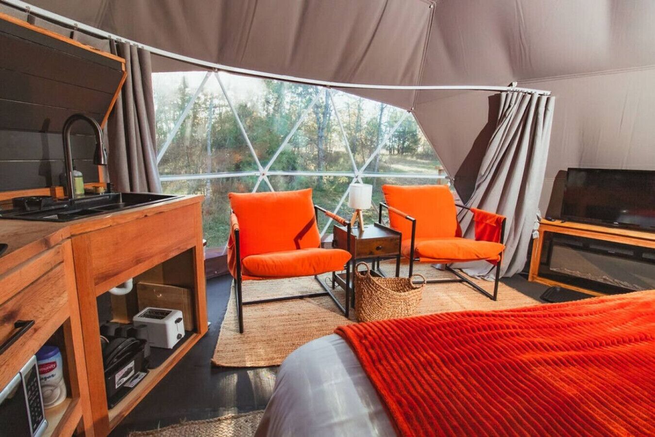 Un alloggio in tenda con angolo cottura, due poltrone arancioni, una TV e vista sugli alberi.