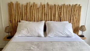 Una cama con sábanas blancas, dos almohadas y un cabecero de listones de madera verticales.