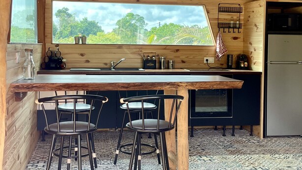 Una cocina de madera con un ventanal grande, dos taburetes de bar y un refrigerador.