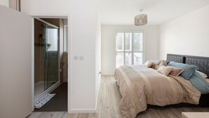 Ein Schlafzimmer mit Bett, einer Duschkabine aus Glas und einem Fenster mit Jalousien.