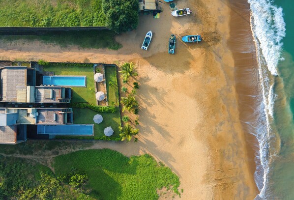 Een strandhuis met zwembad, diverse boten en een zandstrand.