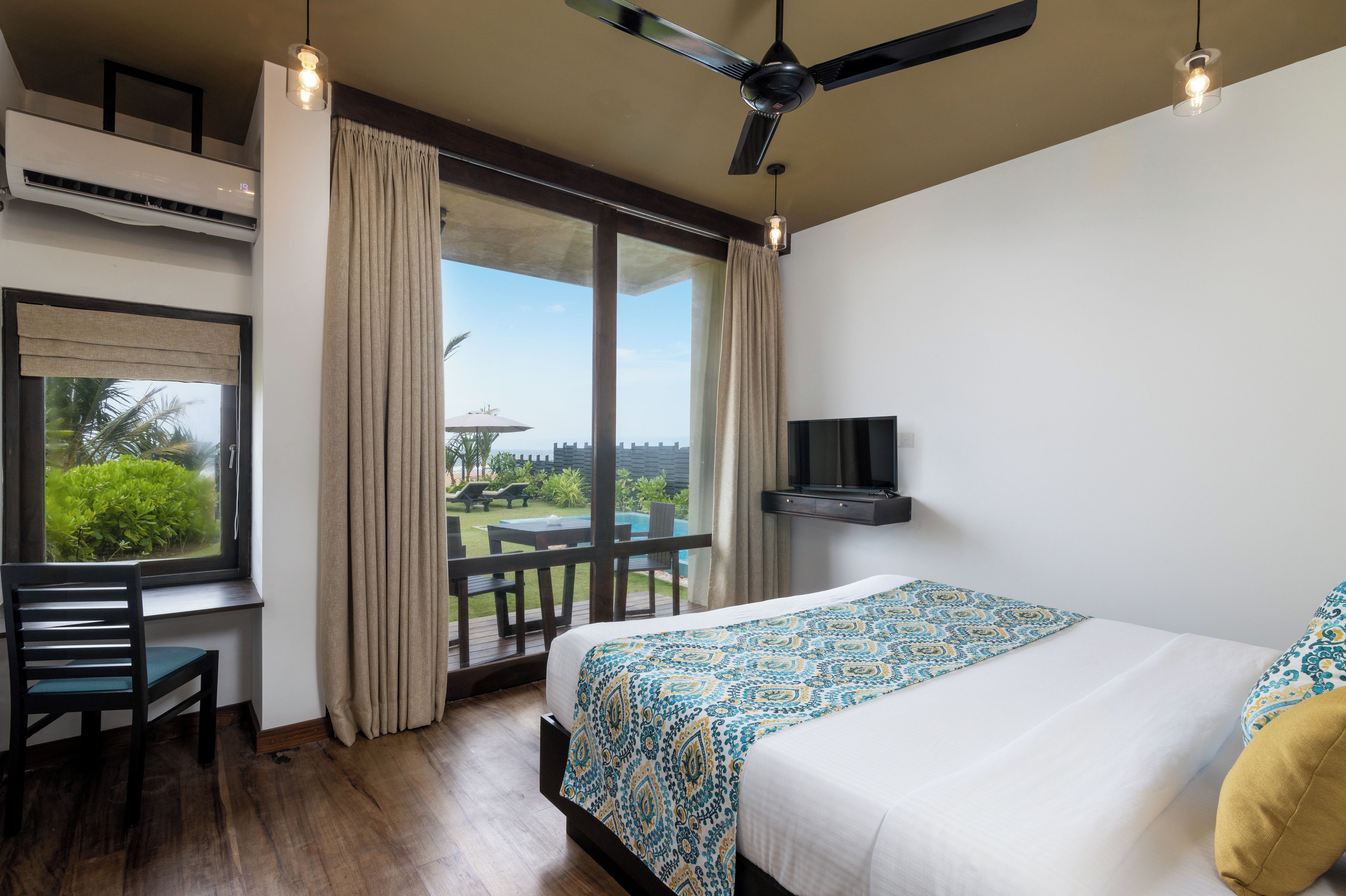 Een hotelkamer met een bed, een bureau, een stoel, een televisie en een balkon met uitzicht.