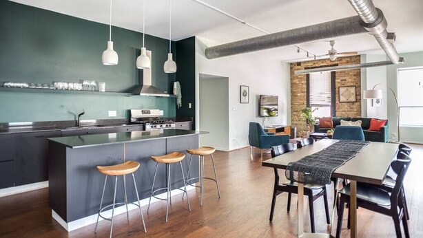 A modern kitchen with a central island, bar stools, pendant lights, and a dining area with a long table and chairs. - Luxury Downtown Penthouse with Private Rooftop! (Chicago)