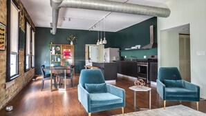 A modern living room with two teal armchairs, a dining table, and a kitchen area with a stove and refrigerator. - Luxury Downtown Penthouse with Private Rooftop! (Chicago)