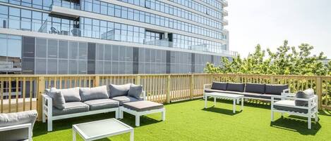 An outdoor patio with a modern building in the background, featuring a seating area with sofas and tables.