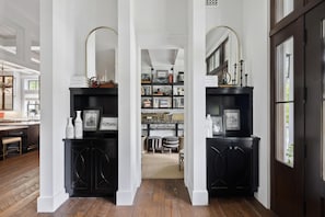 A hallway with black cabinets, a mirror, and a bookshelf with various items.