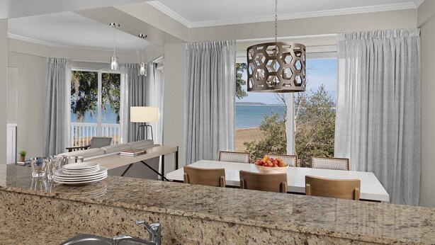 Una cocina moderna con encimeras de granito, un comedor con vistas a la playa y una lámpara colgante.