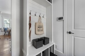 Ein Flur mit weißer Wand, einer Tür und einer Bank, an der eine Tasche hängt.