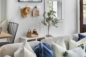 Ein gemütliches Wohnzimmer mit einem weißen Sofa, einem kleinen Holztisch und einer Topfpflanze.