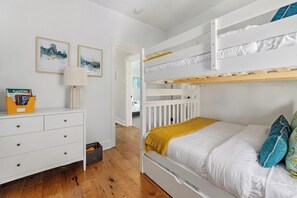 Une chambre avec un lit superposé, une commode blanche, une lampe et des œuvres d’art accrochées au mur.