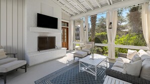 A covered outdoor living area with a fireplace, seating, and a TV mounted on the wall. - Luxe Retreat with Carriage House & Water Views (Bluffton)