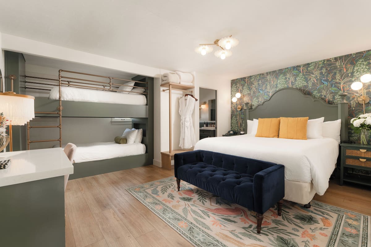 A bedroom with bunk beds, a large bed with a tufted headboard, a bench, a desk, and a mirror.
