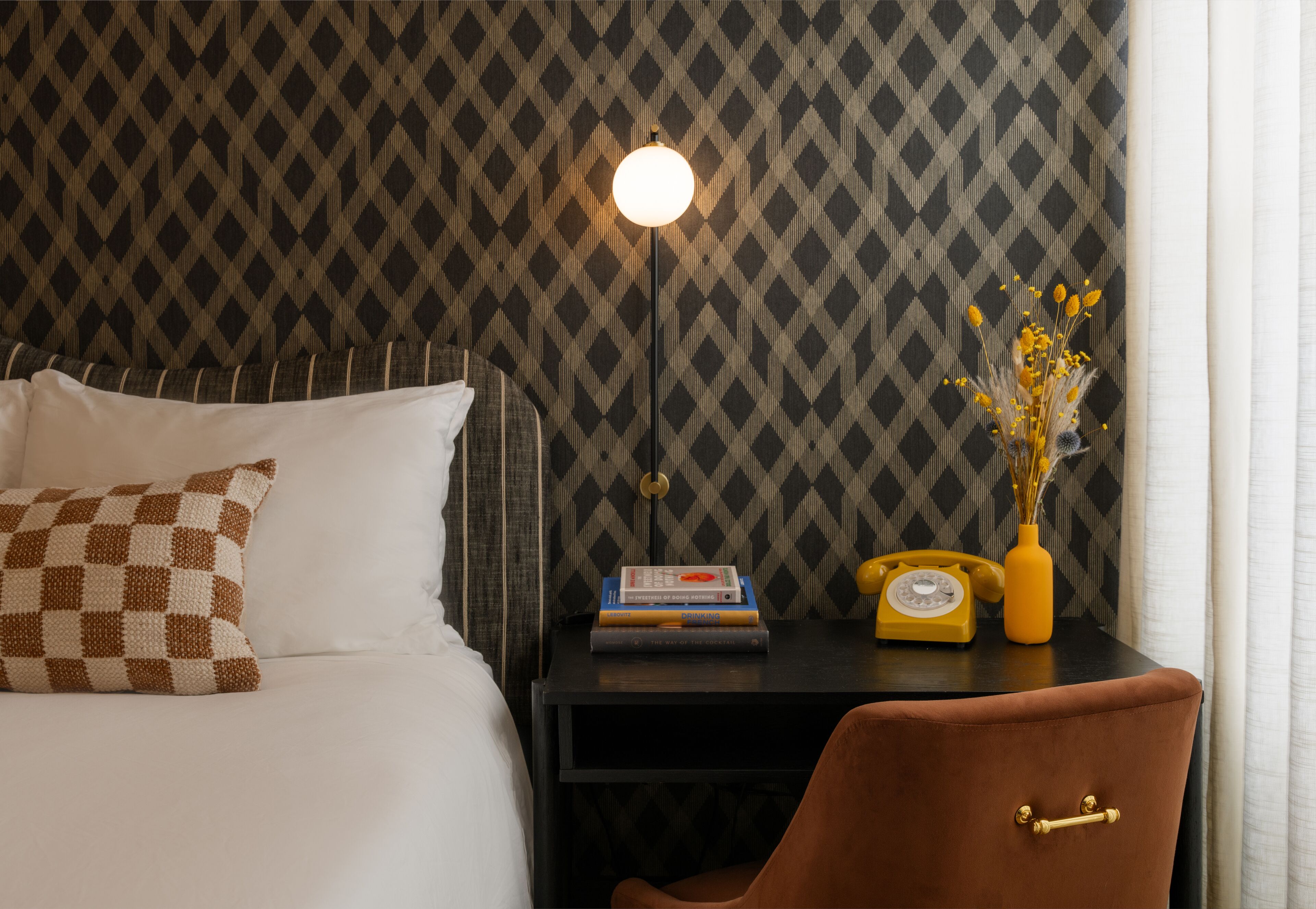 Un lit bien fait, avec des oreillers, une table de chevet avec une lampe, une petite chaise et un vase décoratif rempli de fleurs.