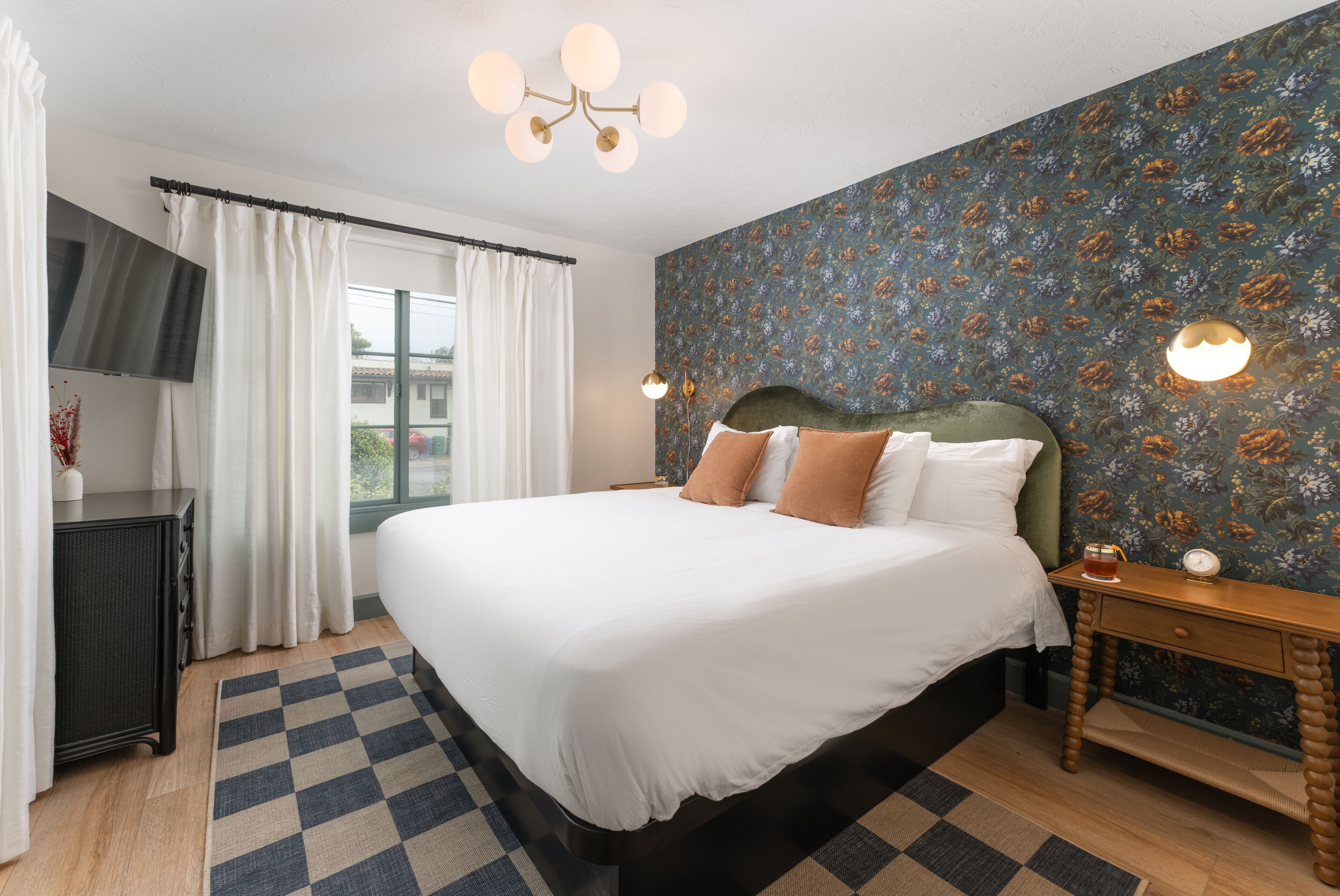 A bedroom with a large bed, a nightstand, a dresser, and a window with curtains.