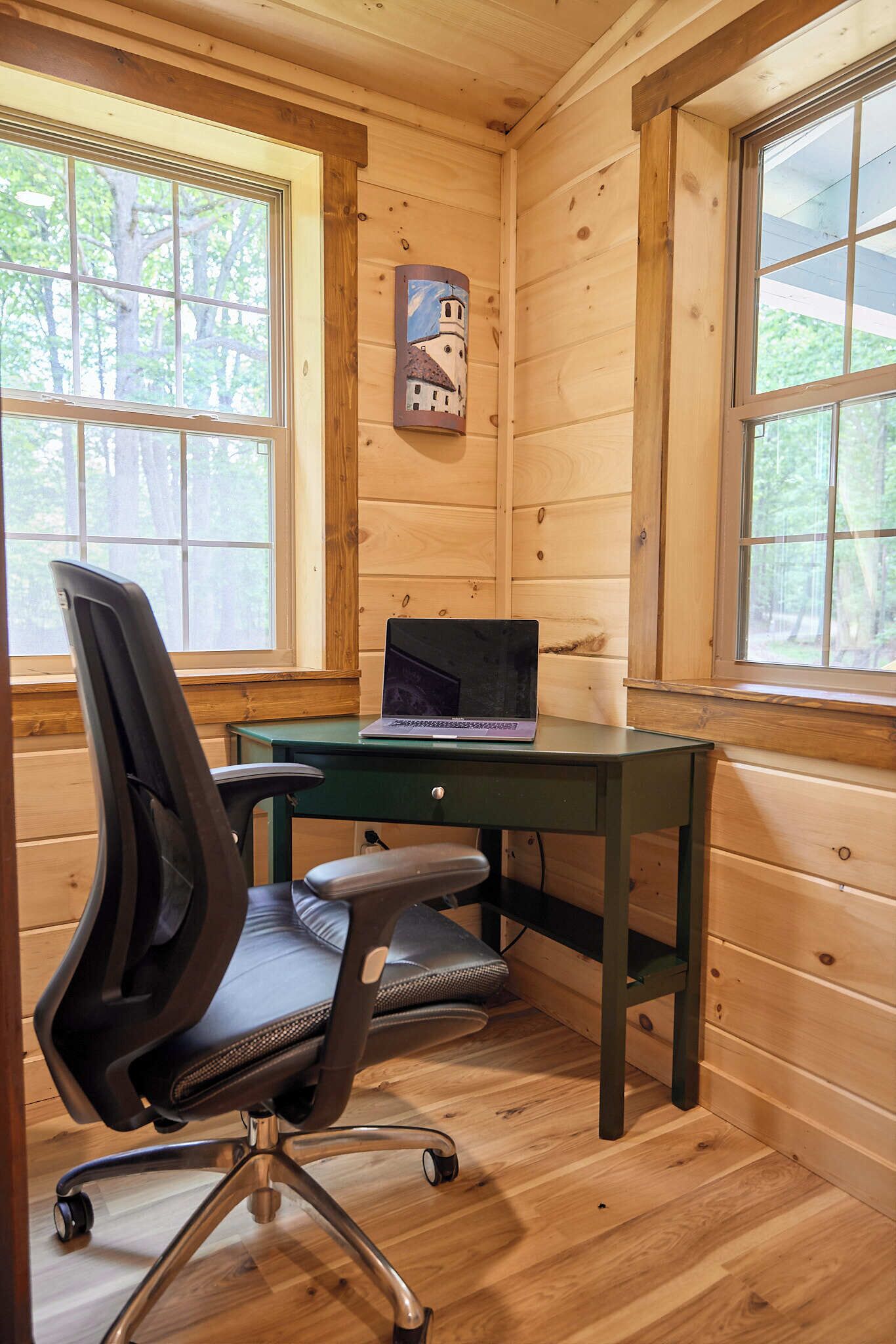 A wooden cabin room with a desk, chair, and laptop.