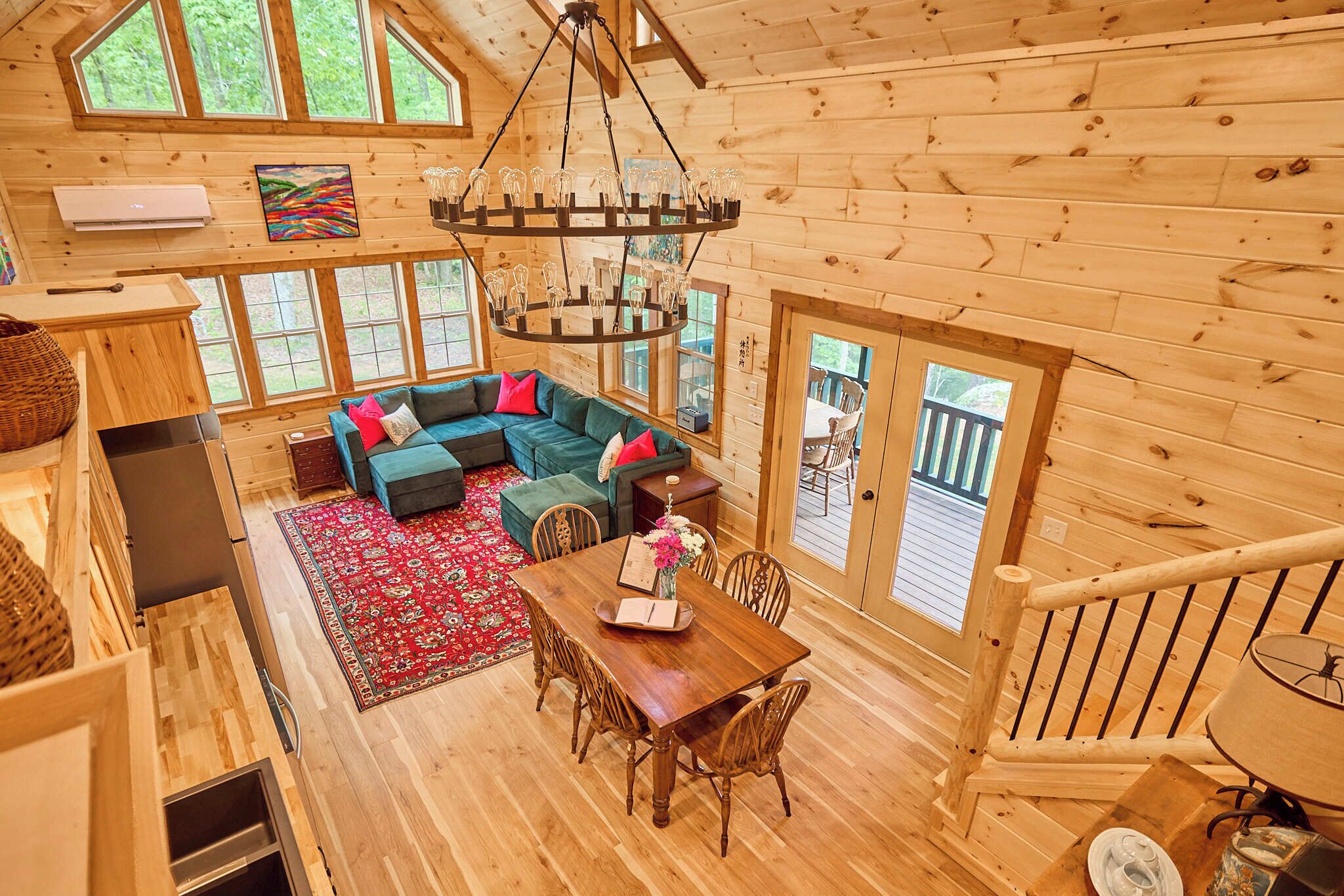 L’intérieur d’un chalet en bois comprend un coin repas, un canapé avec des coussins, un lustre et de grandes fenêtres.
