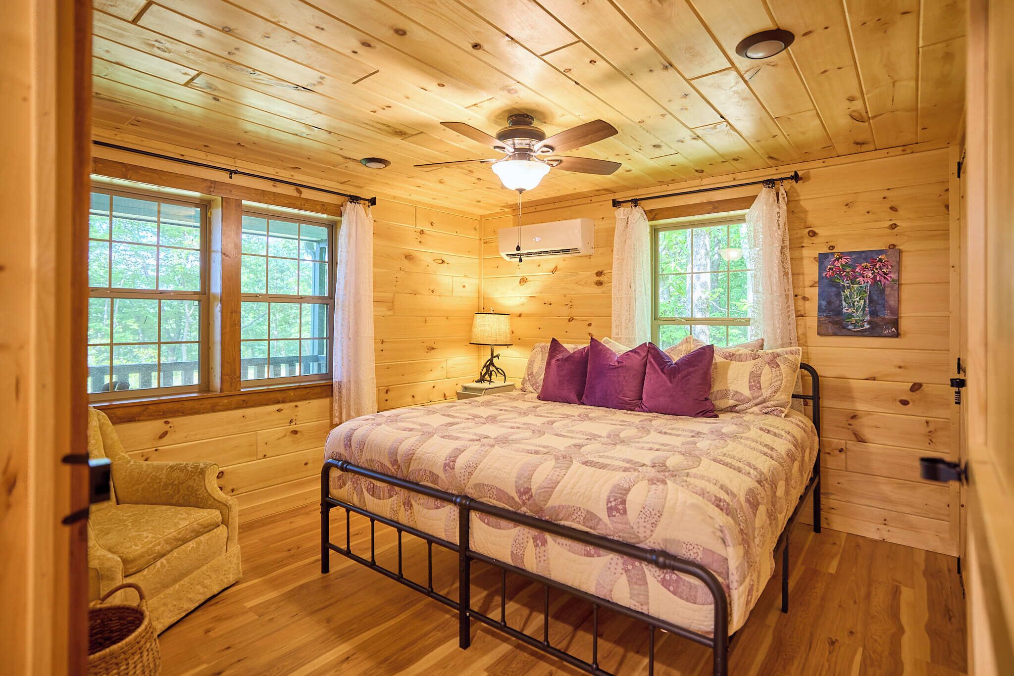 Une chambre dans une cabane en bois, avec un lit, une chaise, une lampe et un tableau accroché au mur.