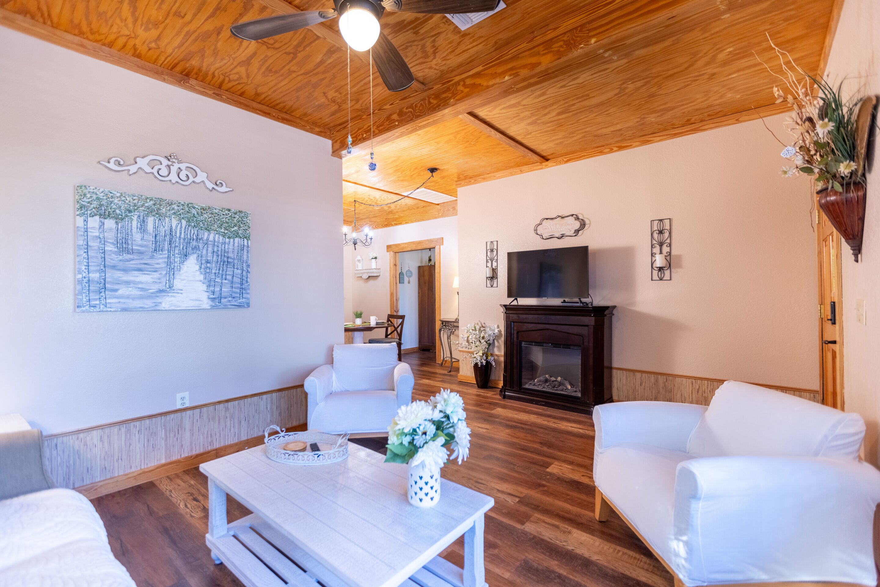 A living room with white furniture, a wooden ceiling, and a fireplace.