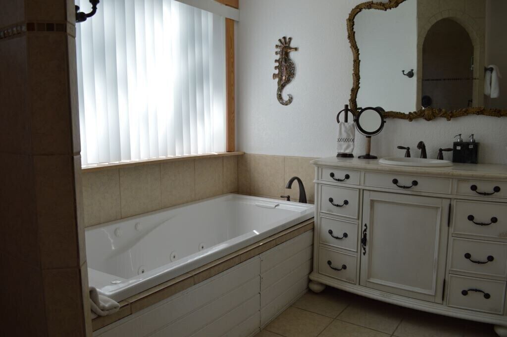 Casa de banho com uma banheira grande, toucador com várias gavetas, espelho e um cavalinho-marinho decorativo na parede.
