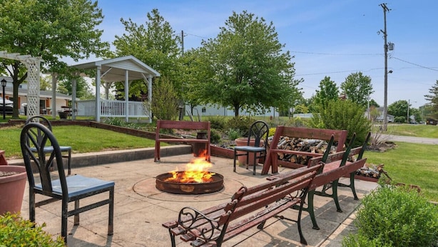 Un patio al aire libre con un pozo de fuego, bancos y sillas de madera.