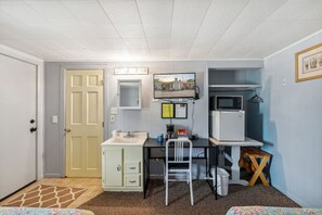 Ein kleines Zimmer mit Küchenzeile, Schreibtisch, Stuhl und Fernseher.