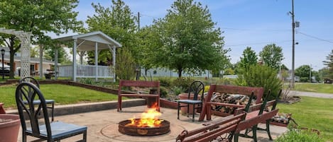 An outdoor patio with a fire pit, wooden benches, and chairs.