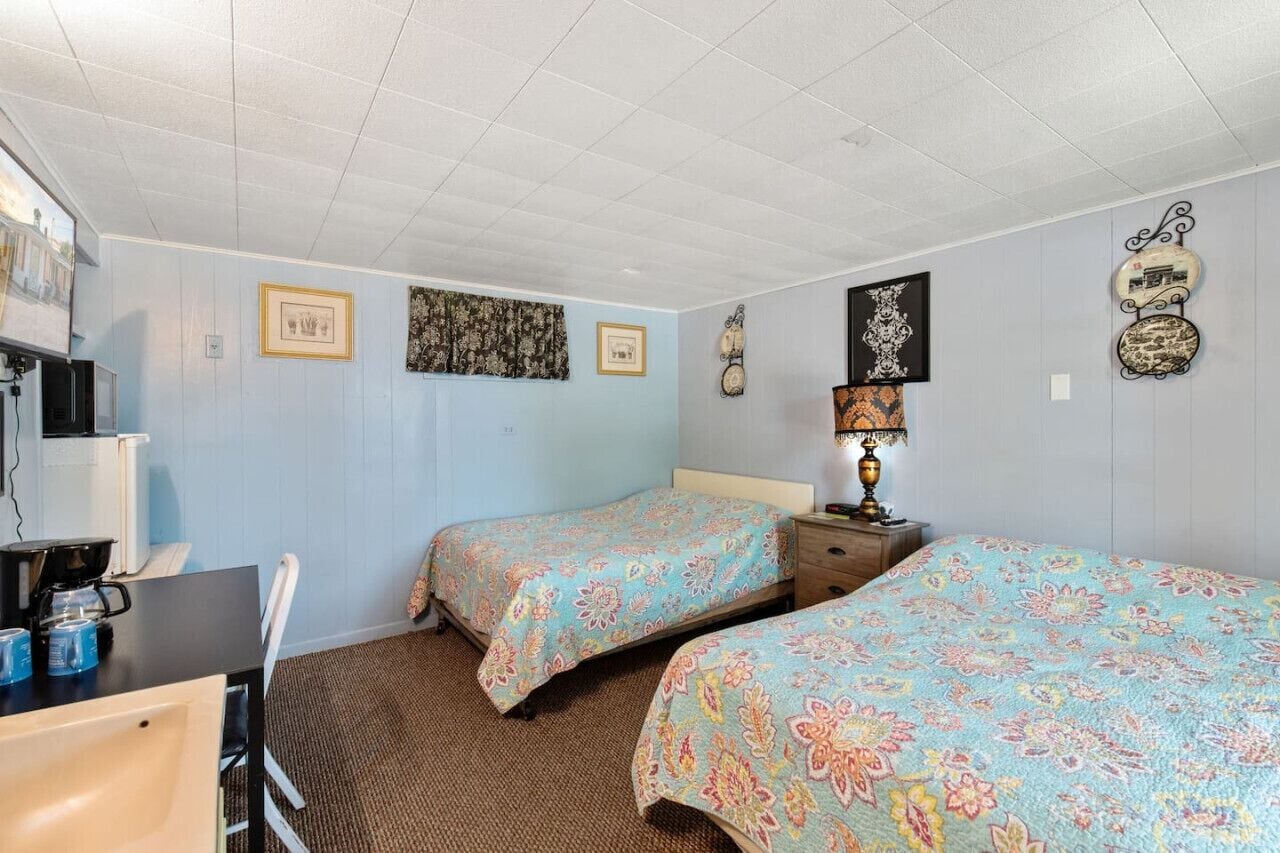 Quarto de hotel com duas camas, uma escrivaninha com computador e uma cafeteira.