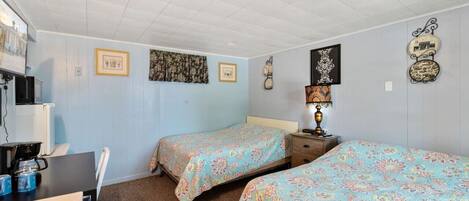 Quarto de hotel com duas camas, uma escrivaninha com computador e uma cafeteira.