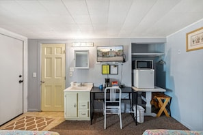 Ein kleines Zimmer mit Küchenzeile, Schreibtisch, Stuhl und Fernseher.
