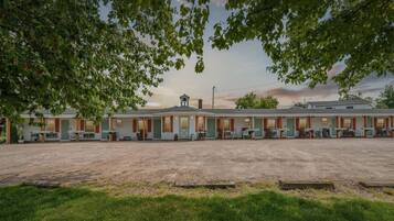 A motel with a central building and attached units, a gravel parking area, and trees framing the scene.