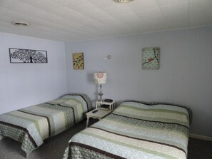 Ein Zimmer mit zwei Einzelbetten, einem Nachttisch mit Lampe und Wandbildern.
