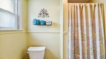 A bathroom with a white toilet, a decorative wall piece above it, and a patterned shower curtain.