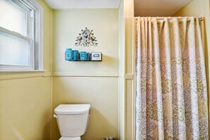 Ein Badezimmer mit einer weißen Toilette, einer Wanddekoration darüber und einem duschvorhang mit Muster.