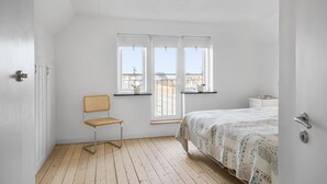 A bedroom with a bed, a chair, a nightstand, and a window with a view of buildings.