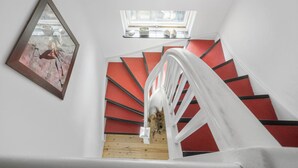 A staircase with red steps and white railings, a framed artwork on the wall, and a window above.