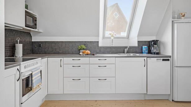 A modern kitchen with white cabinets, a built-in oven, a microwave, a coffee maker, and a window with a view of a brick building.