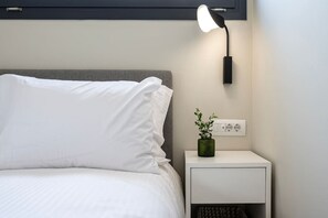 A neatly made bed with white linens, a bedside lamp, and a small green plant on a white nightstand.