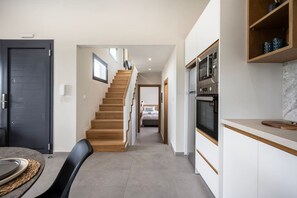 Une cuisine moderne dotée d’appareils électroménagers intégrés, un coin repas avec une table et des chaises, et un escalier menant à une chambre.