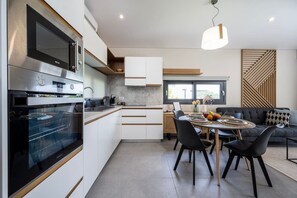 A modern kitchen with built-in appliances, a dining area with a round table and chairs, and a living room with a sofa and decorative pillows.