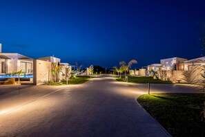A modern residential area with well-lit pathways, contemporary houses, and a swimming pool.