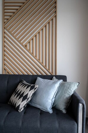 Un canapé de couleur sombre, agrémenté de trois coussins, dont un avec un motif noir et blanc, est placé contre un mur orné d’un panneau en bois à motifs géométriques.