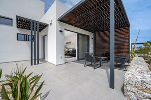 A modern house with a covered patio, a stone wall, and a view of the interior.